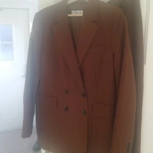 Brun kostym från MNG, stl 44 - Säljer en snygg brun kostym från MNG i storlek 44. Kavajen är dubbelknäppt med klassisk krage och raka fickor, byxorna har rak passform. Perfekt för dig som vill ha en stilren och modern look. Materialet känns mjukt och följsamt.
