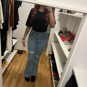 Blå bootcut jeans med slitningar - Snygga ljusblå bootcut jeans med hög midja och slitna detaljer på låret. Jeansen har klassisk femficksdesign och är tillverkade i denim med lite stretch för skön passform. Perfekta för dig som gillar en trendig och avslappnad look.