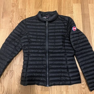 Svart pufferjacka från Colmar - Säljer en svart pufferjacka från Colmar Originals med diskret logga på ärmen. Jackan har horisontella sömmar, dragkedja framtill och grått foder. Perfekt för kyliga dagar och har en clean, sportig look. 