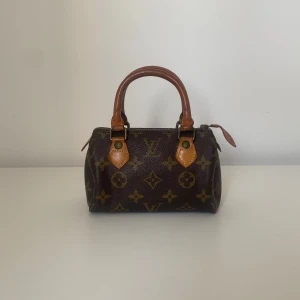 Louis Vuitton Speedy Mini monogram handväska - Säljer en klassisk Louis Vuitton handväska i brunt med ikoniskt monogrammönster och detaljer i ljusbrunt skinn. Väskan har två rundade handtag och dragkedja upptill. Perfekt storlek för det viktigaste och en riktig statement piece.