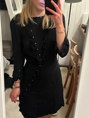 Svart kortklänning Les Coyotes de Paris - Svart kortklänning från Les Coyotes de Paris med snygga volangdetaljer och små pärlor längs en diagonal omlottliknande söm. Klänningen har trekvartsärm och rund hals. Materialet känns lätt och mjukt, perfekt för dig som gillar stilrena och coola plagg. Använd endast 1 gång!🙌✨❤️Tyvärr lite för lite för mig, storlek 14 år, men passar XXS-XS💖