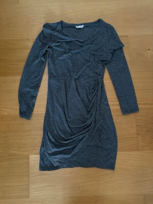 Mörkgrå långärmad klänning Cubus - Snygg mörkgrå klänning från Cubus i storlek 146/152. Modellen är kort med långärmade och har en cool drapering på framsidan som ger en extra touch. Materialet känns mjukt och stretchigt, perfekt för dig som gillar bekväma plagg med lite edge. 50% polyester, 50% Viskos. 