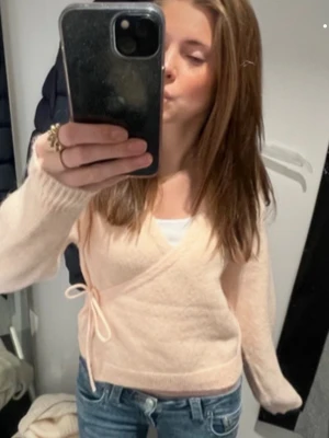 Snygg tröja  - Superfin stickad omlotttröja från Lindex i en mjuk ljusrosa/persikofärg som är både trendig och lätt att matcha. Tröjan är i princip ny och i mycket fint skick utan fläckar eller slitage. Omlottdesignen med knytning i sidan ger en feminin och stilren look och funkar lika bra till jeans som till kjol. Storlek XS, och sitter väldigt fint på. Säljer då den tyvärr inte kommer till användning! Skriv för fler bilder!!🤗🤗