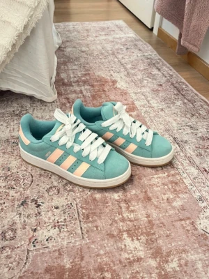 Adidas campus 00’s  mintgrön/ljusrosa 36⅔ - Säljer ett par snygga Adidas sneakers i mintgrönt med ljusrosa ränder och vit snörning. Skorna har en klassisk rund tå, platt gummisula och är tillverkade i mocka med textilfoder. Passar 37