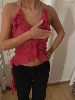 Rosa topp med volanger från zara - Säljer en rosa topp med volanger och halterneck-knytning. Toppen är ärmlös och har öppen rygg, plisserad struktur och långa volangdetaljer längs sidorna💋inte använts
