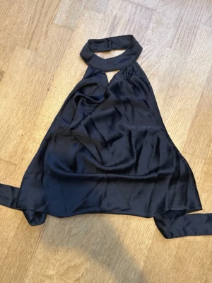 Svart halterneck topp i satin - Säljer denna jättefina fest topp med öppen rygg och med knytning i ryggen.
