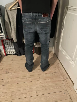 Jacob Cohën mörkblå/grå jeans straight fit - Snygga mörkblå jeans från Jacob Cohën med klassisk femficksdesign och raka ben. Jeansen har subtila slitningar, kontrastsömmar och en brun patch med logga bak. Materialet är mjuk och slitstark denim i bomull. Perfekt för dig som gillar stilrena och exklusiva jeans.