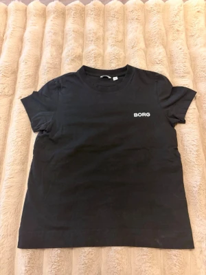 Svart t-shirt från Björn Borg - Svart t-shirt från Björn Borg i storlek XS. Klassisk rund hals och korta ärmar, med vit BORG-logga på bröstet. Tillverkad i mjuk bomull som är skön mot huden. Perfekt för dig som gillar enkel stil för träning. aldrig använd!! 