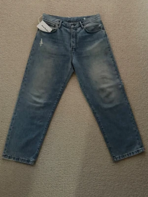 Blå Acne Studios jeans 1991  - Säljer ett par riktigt snygga blå jeans från Acne Studios model 1991. Jeansen har slitnings detaljer vid fickorna och klassisk femficksdesign. Materialet är 100% bomull och färgen är ljusblå med tvättade partier för en lite vintagekänsla. Back taben är i riktigt fint läder och är präglad med acne studios loggan. Jeansen är helt autentiska och är köpta i cph. Orginal lapp medföljer, även orginal jenans bälte medföljer. Ny pris ligger på 5000kr 