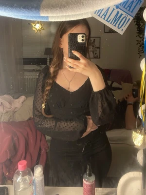 Svart prickig blus från FASSIER XS - Säljer en svart blus från FASSIER i storlek XS. Toppen har transparenta långärmar med prickigt mönster och en croppad passform. Framtill finns knappar och en snygg v-ringad urringning. Perfekt för dig som gillar trendiga detaljer och stilren look.