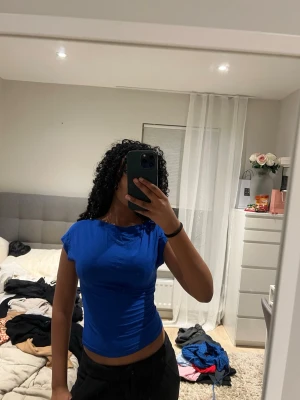 Blå croppad topp med öppen rygg - Säljer en blå croppad topp med korta ärmar och öppen rygg. Toppen är figurnära och har en enkel, stilren design utan mönster. Perfekt för dig som gillar en lite mer vågad look. Materialet känns mjukt och stretchigt, troligen polyester eller bomull.