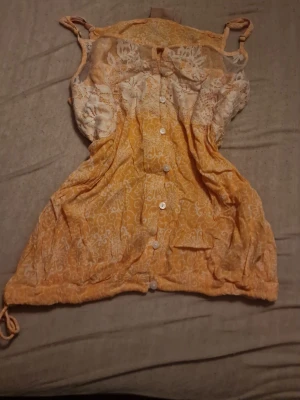 Orange blus med broderi - Helt oanvänd, prislapp saknas. Jätte fin och har ett unikt broderi på bröstet, perfekt för dig som vill sticka ut lite och ha en vintage look. På bröstet finns knappar och längst ner finns trådar då du kan skjustera hur den sitter. Gjord av 100% viskos vilket innebär ingen polyester för dig som kan vara allergisk! Priset kan diskuteras🫶