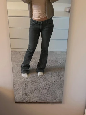 Mörkgrå bootcut jeans med låg midja - Säljer ett par svarta jeans med bootcut-modell och låg midja. Jeansen har klassisk femficksdesign och är i ett mjukt denimtyg. Snygg passform som sitter tajt upptill och släpper ut vid bensluten. Perfekta till sneakers eller boots.