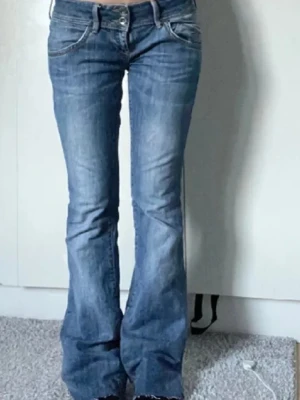 Tommy Hilfiger bootcut jeans blå - Säljer ett par blå Tommy Hilfiger Sonora Bootcut jeans i modellen Alabama Stretch. Jeansen har klassisk femficksdesign, låg midja och bootcut-ben. Materialet är stretchigt jeans för extra komfort och passform. Perfekta för dig som gillar en avslappnad men snygg look. Hon på bilden är 170 cm