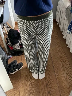 Mönstrade vida byxor med resårmidja - Säljer ett par riktigt snygga byxor med grönt rutmönster och bred, grön resår i midjan. Byxorna har en rak och vid passform som ger en chill vibe. Materialet känns mjukt och stretchigt, perfekt för dig som gillar bekväma men ändå trendiga plagg.