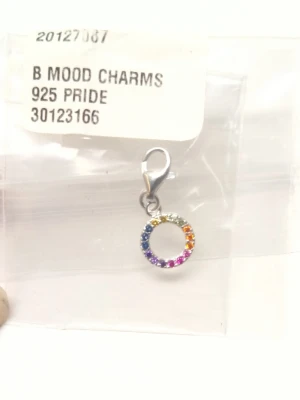 Regnbågsfärgad charm i silver - Snygg rund charm i äkta silver med gnistrande stenar i regnbågens alla färger. Perfekt att hänga på armband, halsband eller väska för en färgglad touch. Enkel att fästa med karbinhake. Mood charms från Guldfynd. Helt ny i fortfarande i förpackning.