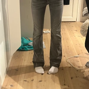 Grå bootcut jeans med detaljer - Snygga grå jeans med bootcut passform och coola detaljer på bakfickorna. Jeansen har låg midja och är aldrig använda. 33 cm i midjemått rakt över och ca 80 cm i innerbenslängden.