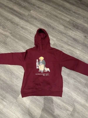 Helt oanvänd raulph louren hoodie - Vinröd hoodie från Polo Ralph Lauren med det klassiska Polo Bear-trycket framtill. Mjuk och bekväm med huva samt ribbade muddar för bra passform. En stilren hoodie med ikonisk design och hög kvalitet.