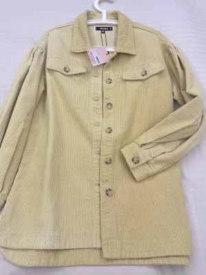 Beige manchester overshirt från Missguided - Säljer en oversized beige overshirt från Missguided i mjuk manchester. Jackan har stora knappar framtill, två bröstfickor med lock och klassisk krage. Perfekt lager på lager-plagg för dig som gillar en chill och trendig stil.