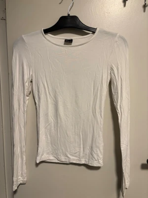 Vit långärmad topp i bomull - En enkel och stilren vit långärmad topp från Monki. Modellen har rund halsringning och är gjord i mjuk bomull som känns skön mot huden. Perfekt att matcha med jeans eller kjol för en clean look.