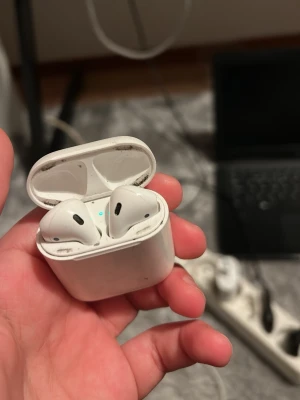 Apple AirPods (2nd Generation) - Apple AirPods med laddningsetui. Trådlösa hörlurar med enkel anslutning till iPhone. Skick: Synligt smuts och slitage på etui och insida, men fungerar. Perfekt för dig som vill ha prisvärda AirPods till vardagsbruk. Säljer dem för behöver pengar