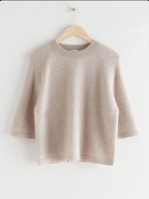 Beige stickad tröja från & Other Stories - Mysig beige stickad tröja från & Other Stories. Tröjan har rund hals, trekvartsärm och en loose passform. Materialet är mjukt och fluffigt, vilket gör den extra skön att ha på sig.