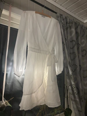 Vit omlottklänning från Bubbleroom - Säljer en vit omlottklänning från Bubbleroom i storlek 36. Klänningen har långa, transparenta ärmar, volangdetaljer nertill och knyt i midjan. Den är kort och har en v-ringad design som ger en fräsch och stilren look. Perfekt för dig som gillar romantiska och trendiga plagg. Endast använd en gång inga defekter. Passar perfekt till skolavslutning eller studenten💞
