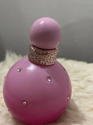 Rosa parfymflaska med strass - BRITNEY SPEARS PARFYM - En helt full vanilj-frukt Snygg rosa parfymflaska dekorerad med små strasstenar och ett glittrande halsband. Perfekt för dig som gillar trendiga och unika detaljer på din parfymhylla.