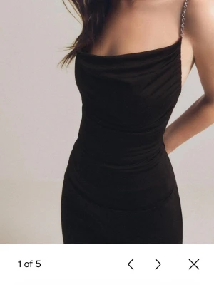 Svart linnetopp med kedjeband - Säljer en svart linnetopp med tunna kedjeband och draperad front. Toppen har asymmetrisk nederkant och sitter snyggt figurnära. Perfekt att styla med jeans eller kjol för en trendig look.