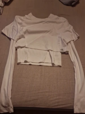 Vit croppad topp från Calvin Klein Jeans - Säljer en vit croppad topp från Calvin Klein Jeans i storlek XS. Toppen har långa ärmar och är tillverkad i mjuk bomull. Den har en stilren design med ribbad nederkant och diskret CK-logga på sidan. Perfekt att matcha med höga jeans eller kjol. Passar även bra till träning/gympa eftersom den är väldigt skön, helt oanvända, aldrig haft på mig. Köpt för 500, säljer för 400, pris kan diskuteras. Intresserad? Kontakta om du vill veta hur den sitter på🫶
