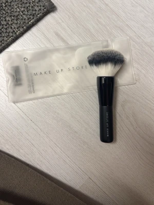 Sminkborste från Make Up Store - Säljer en fluffig sminkborste från Make Up Store med svart handtag och mjuka borststrån i svart och vitt. Den är liten och smidig och ska användas till puder. Aldrig använd