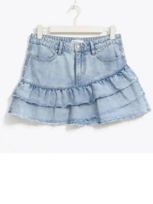 Ljusblå jeanskjol med volanger - Säljer en ljusblå jeanskjol med volang. Kjolen har klassiska fickor fram och bak samt knapp och dragkedja i midjan. 