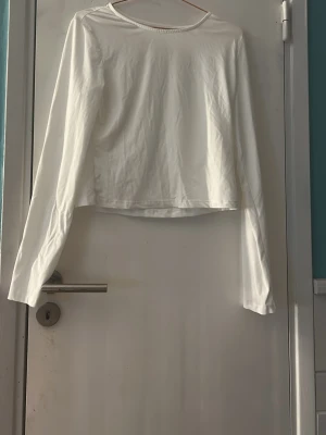 Vit långärmad topp i bomull - Enkel och stilren vit långärmad topp med rund halsringning. Toppen är croppad och har en rak passform, perfekt att matcha med jeans eller kjol. Tillverkad i mjuk bomull som känns skön mot huden. Använd en gång så den är som ny. Stl xl men passar även L och M