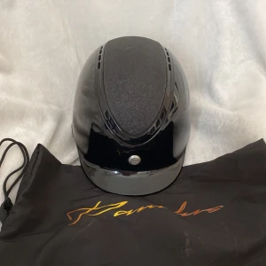 Svart ridhjälm från Pandus, strl S - Snygg svart ridhjälm från Pardus med blank finish och ventiler upptill. Den har  lite skador och några repor som gör att den säljs lite billigare. Andvänd i ett år.  Den levererars med fodral. Inlägget tvättas innan skickning❤️ Nypris 2300kr.