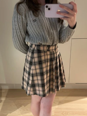 Rutig högmidjad kjol Hollister Strl S - Supersnygg plisserad kortkjol med ljusrosa och svart rutigt mönster. Kjolen är högmidjan och har en dragkedja på sidan. Knappen framtill är dekorativ.