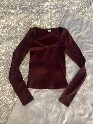 Vinröd topp - Söt vinröd långärmad ribbad topp med spetsdetaljer och en rosett vid bysten. Inga defekter och är i utmärkt skick!  Kolla gärna in mina andra annonser och köp gärna bundle, då kan vi komma överens om ett bra paketpris!