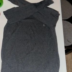 Mörkgrå stickad tröja från Volcom - Snygg mörkgrå stickad tröja från Volcom med diskret logga broderad på bröstet. Tröjan har rund halsringning och långa ärmar, samt ribbade muddar vid ärmslut och nederkant. Perfekt för dig som gillar stilrena och enkla plagg.