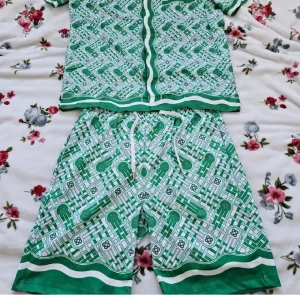 Grön mönstrad skjorta Casablanca - Casablanca Tennis Club skjorta i grönt och vitt med grafiskt rutigt mönster och detaljerade linjer. Kortärmad med klassisk krage, bröstficka och knappar framtill. Materialet är mjukt och lätt, perfekt för sommarens chill. Snyggt matchad med shorts i samma stil.