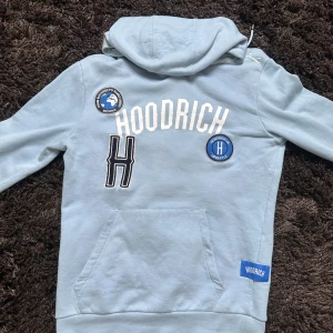 Ljusblå hoodie från Hoodrich - Snygg ljusblå hoodie från Hoodrich med broderade patches och tryck på framsidan. Stor ficka framtill och huva med snörning. Hoodrich-logga och texten 'From nothing to something' på ena patchen. Perfekt för streetwear-stilen.