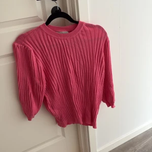 Rosa ribbad tröja från Zink - Superfin rosa ribbstickad tröja från Zink med rund hals och ballongärmar. Tröjan har en snygg struktur och en liten metallbricka med logga vid ärmslutet. Perfekt för dig som vill ha en färgklick i garderoben!