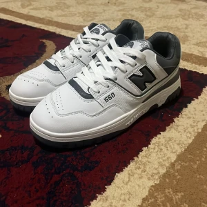 New Balance 550 vita och grå sneakers - Säljer ett par helt nya New Balance 550 sneakers i vitt och mörkgrått. Skorna har klassisk snörning, rund tå och platt sula. Ovandelen är i skinn med detaljer i syntet och mesh. Nypris är 1300 kr. Priset kan diskuteras.