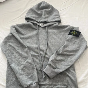 Stone island hoodie  - Light gray Stone Island-style hoodie featuring a soft cotton feel, adjustable drawstring hood, front kangaroo pocket, and ribbed cuffs and hem. It has the signature black and yellow compass logo patch on the left sleeve. Shoulder width 52.5,cm and clothing length 69 cm