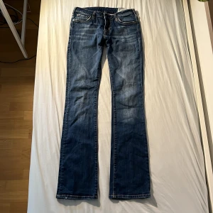 Blå bootcut jeans från Crocker - Snygga blå jeans från Crocker med klassisk bootcut passform. Jeansen har fem fickor, kontrastsömmar och ett brunt läderpatch med logga bak i midjan. Materialet är slitstarkt denim och färgen är mörkblå med lätt tvättade detaljer. Storlek 28/34 vilket är ungefär xs-s 