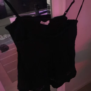 Svart linnetopp med spetsdetalj - Svart linnetopp från Etab. 1999 med smala axelband och smockad överdel. Toppen har en flowy passform och spetsdetalj längst ner som ger en extra touch. Perfekt för varma dagar och enkel att matcha med jeans eller kjol.