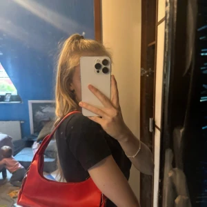 Röd axelväska vintage  - Säljer en snygg röd axelväska med stilren design och glansig. Väskan har en enkel form med bred axelrem som gör den bekväm att bära. Perfekt för dig som vill ha en färgklick till din outfit.