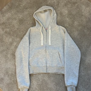 Ljusgrå hoodie från Gina Tricot - Ljusgrå zip-hoodie från Gina Tricot i mjuk bomullsblandning. Tröjan har huva med snörning, dragkedja framtill och stora fickor. Storlek xs. Nypris 330 kr. Köptes förra månaden men har knappt kommit till användning.