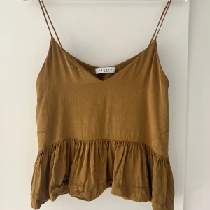 Volanglinne från Sandro Paris - Lite skrynklig på bilderna men en supersnygg linnetopp i en lite senaps gul/guldig färg från Sandro Paris med volang nertill, tunna axelband och v-ringning!