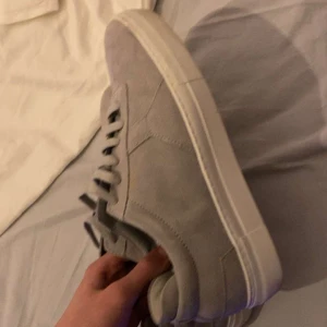 Grå mockasneakers från Axel Arigato - Snygga grå sneakers från Axel Arigato i mjuk mocka med vit platt sula. Skorna har rund tå, snörning och stilren design som passar till jeans eller chinos. Perfekta för dig som gillar minimalistisk stil och vill ha ett fräscht tillskott till garderoben. Skorna är bara använda typ 3 gånger men va inte min stil så väljer därför att sälja dem. Dessa går även inte heller att få tag på längre då axel arigato inte säljer denhär stilen mer.
