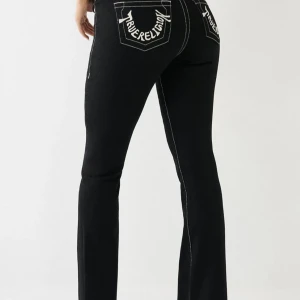 Svarta True Religion bootcut jeans - Svarta jeans från True Religion med kontrasterande vita sömmar och broderade loggor på bakfickorna. Modellen är lågmidjad och har bootcut-ben för en snygg siluett. Jeansen har klassisk femficksdesign och är tillverkade i jeansmaterial.