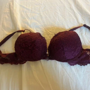 Vinröd spets korsett från Bubbleroom - Säljer denna push up bh  från Cubus  med vacker spets och vadderade kupor. Den har en liten rosett och metallcharm framtill, justerbara axelband och snyggt blommigt spetsmönster över hela. 